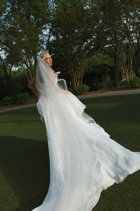 Emma turning in her gown, veil catching the light on the lawn.