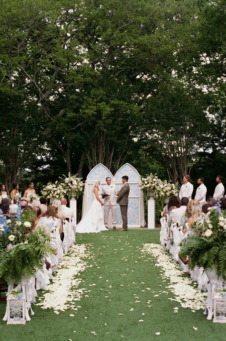 The ceremony from the back of the aisle, petals scattered along the grass.