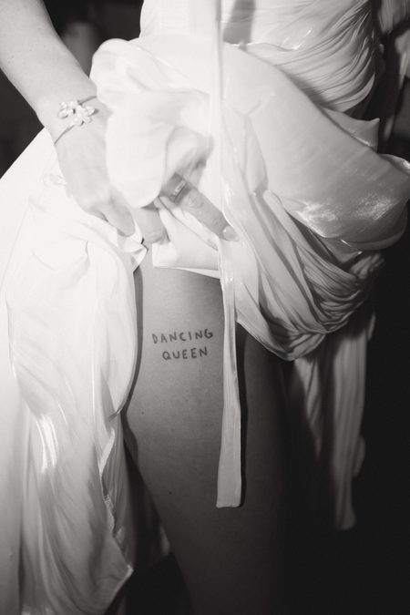 Emma lifting her skirt to show the “Dancing Queen” tattoo on her thigh.