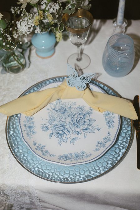 A reception place setting with a blue toile plate and pale yellow napkin.
