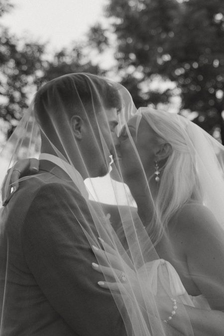 Emma and Philip leaning together beneath her veil, in black and white.