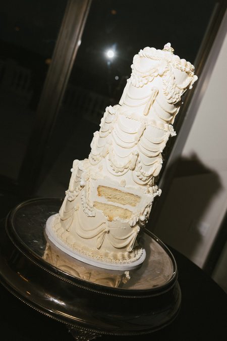 The tiered wedding cake, piped in soft ivory, on a dark stand.