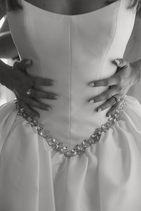 The beaded back of Hunter's gown being fastened, in black and white.