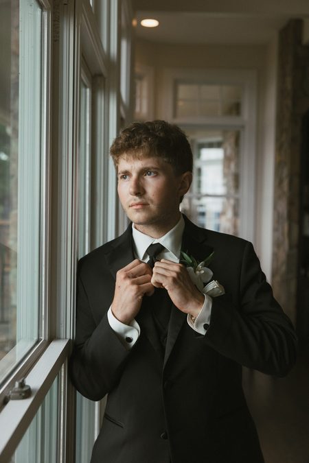 Gavin adjusting his tie beside a window.