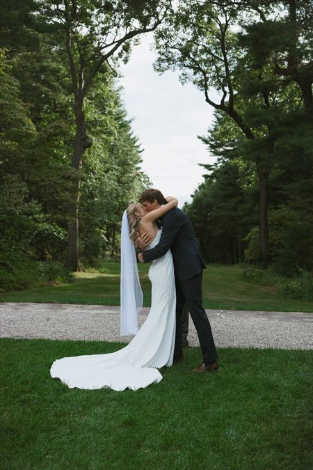 Kendra and Will kissing on the tree-lined grass path after the ceremony.