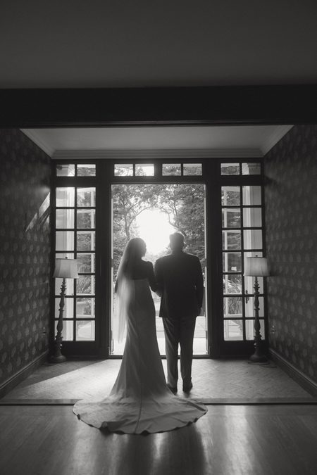 Kendra and Will walking out through the french doors, her train trailing behind, in black and white.