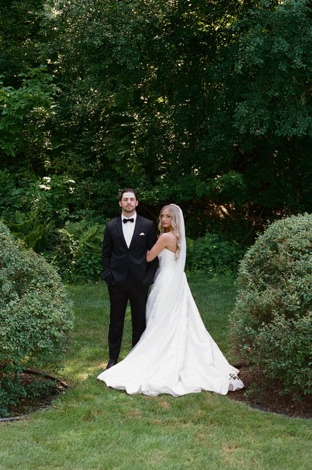 Stephanie and Nick standing together among the garden hedges.