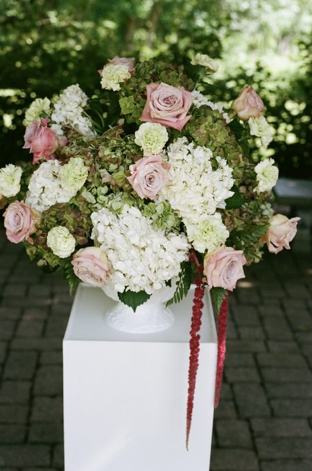 A garden arrangement of roses and hydrangea on a white plinth.