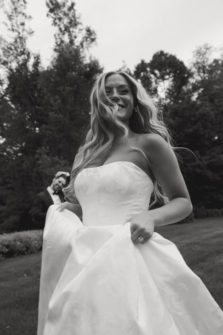 Stephanie laughing as she gathers her skirt, in black and white.