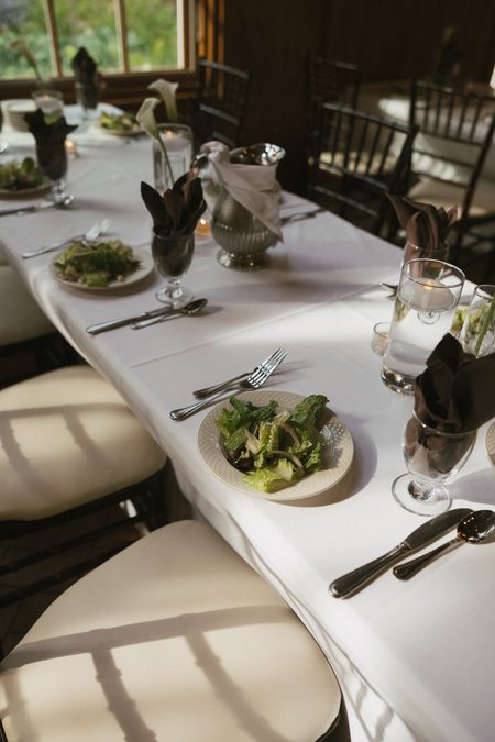 A reception table laid with white linen, greenery and the first course.
